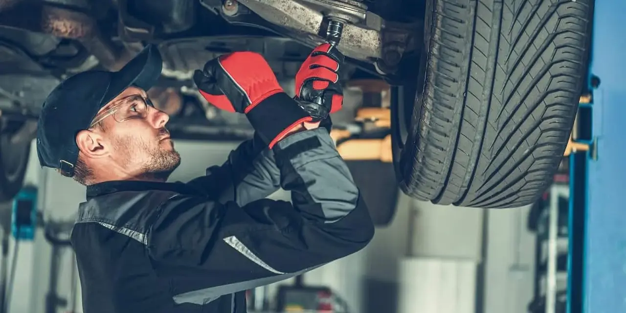 Mechanik w rękawicach dokręca sworzeń zwrotnicy w podwoziu samochodu.