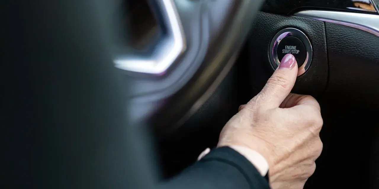 Dłoń naciska przycisk "ENGINE START/STOP". Niestety, samochód nie odpala, co frustruje kierowcę.