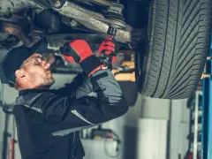 Mechanik w rękawicach dokręca sworzeń zwrotnicy w podwoziu samochodu.