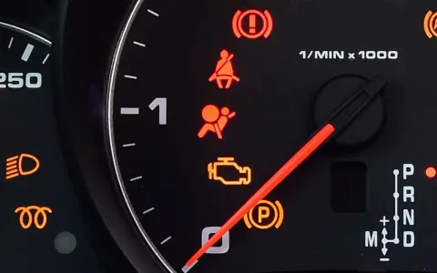 Kontrolka poduszki powietrznej w samochodzie świeci się na pomarańczowo, obok ikony pasa bezpieczeństwa i hamulca ręcznego.