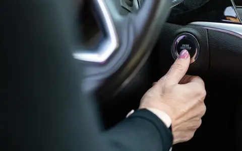 Dłoń naciska przycisk "ENGINE START/STOP". Niestety, samochód nie odpala, co frustruje kierowcę.